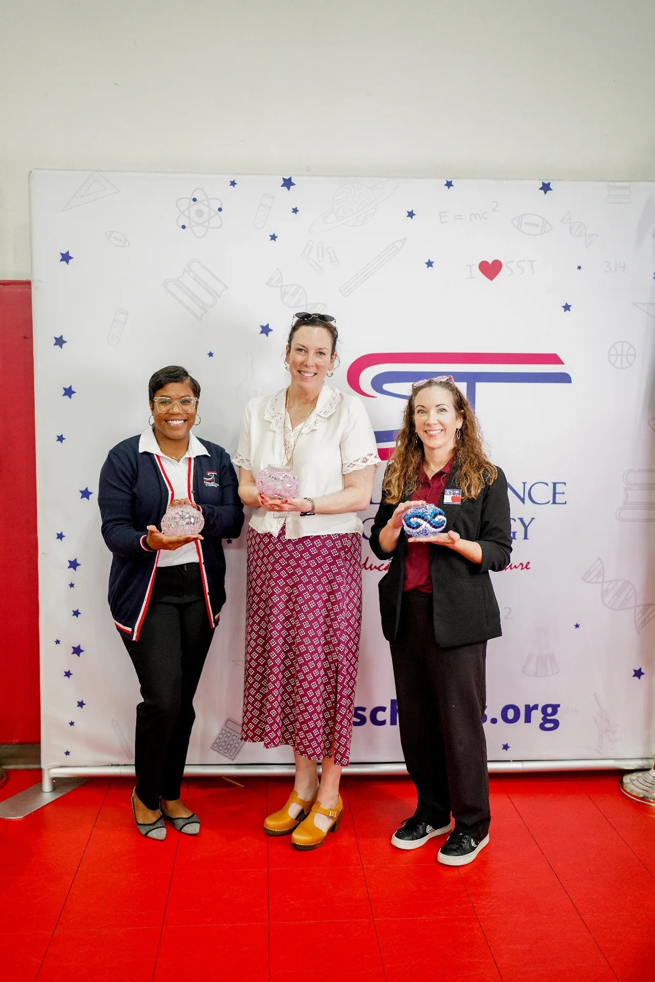 Three women standing in front of a backdrop with a logo and text, holding awards.