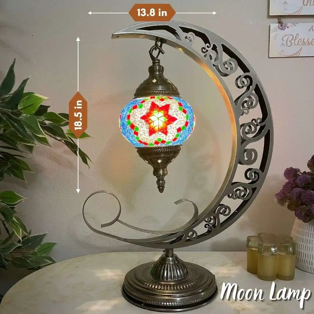 Decorative Turkish Moroccan mosaic moon lamp with colorful glass shade on a white surface, surrounded by plants and candles.