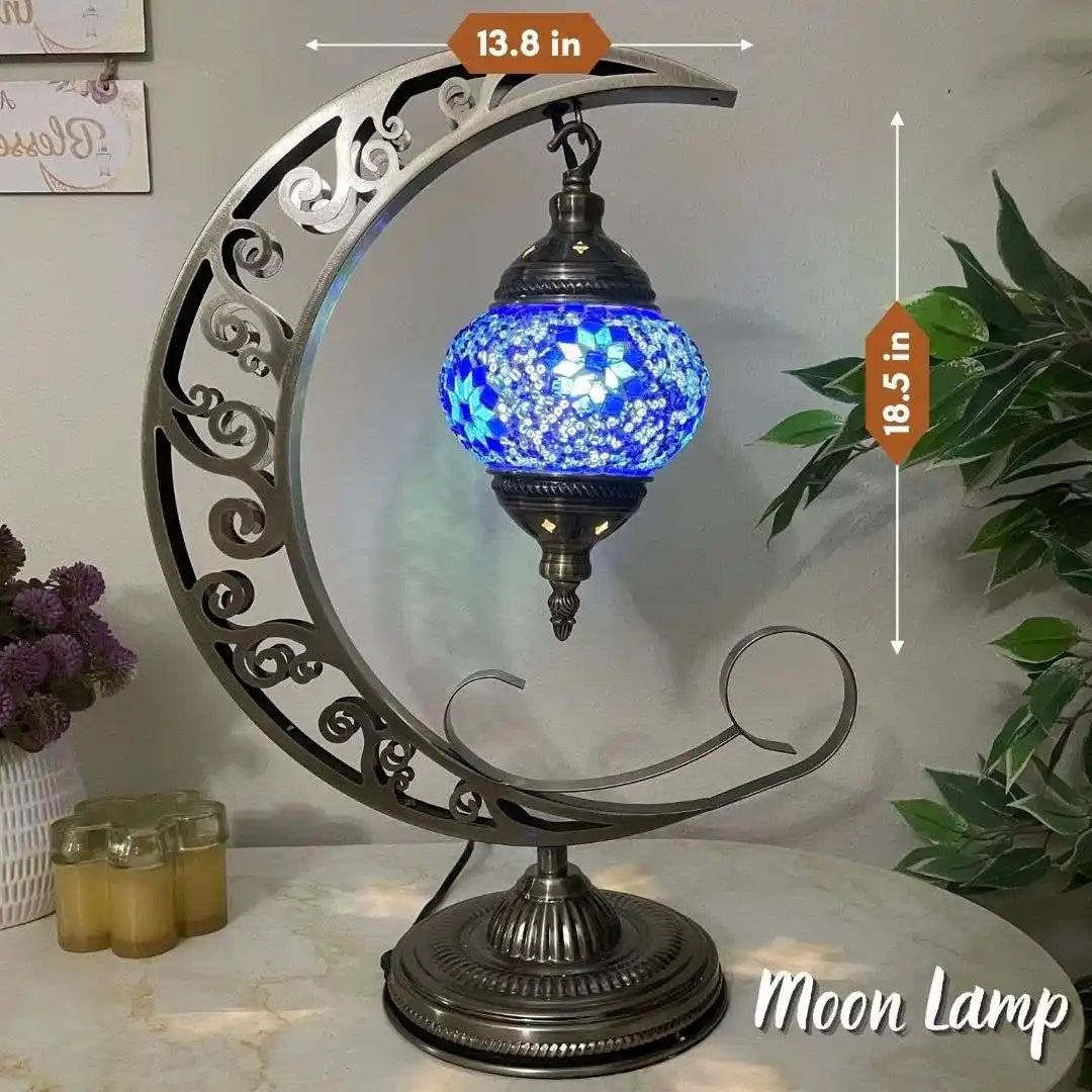 Decorative Turkish Moroccan Mosaic moon lamp with blue glass shade on a marble surface, surrounded by plants and candles.