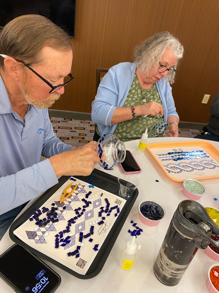 Two people working on a mosaic art project at a table.