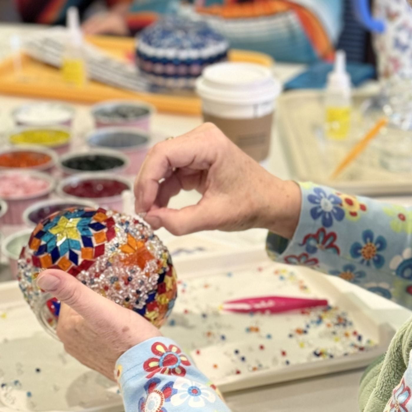 Person holding a colorful mosaic ball with craft materials in the background