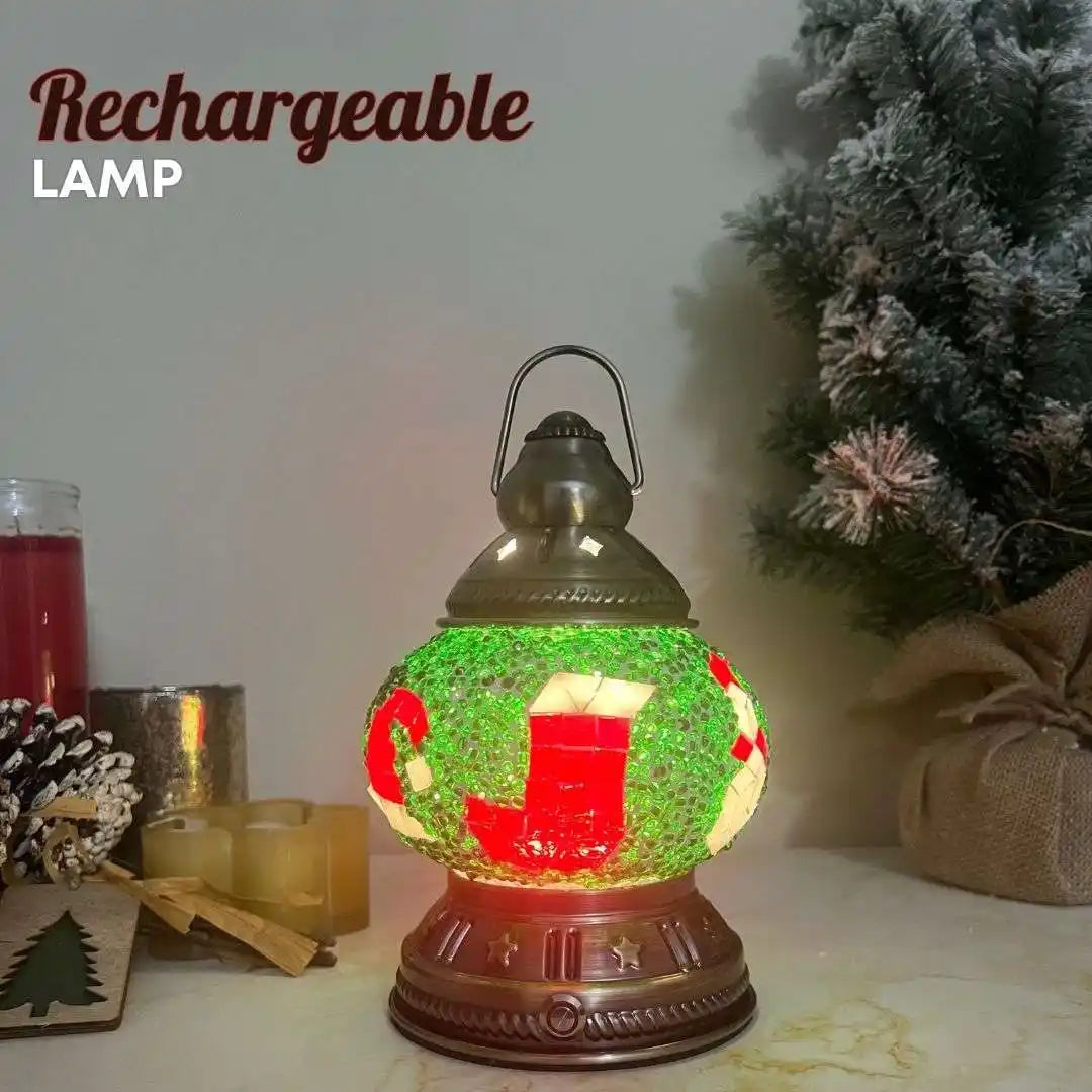 Decorative rechargeable lamp with Christmas design on a table with candles and a tree in the background.