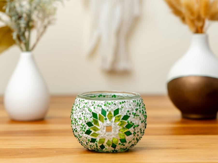 Decorative glass candle holder with green mosaic pattern on a wooden surface.