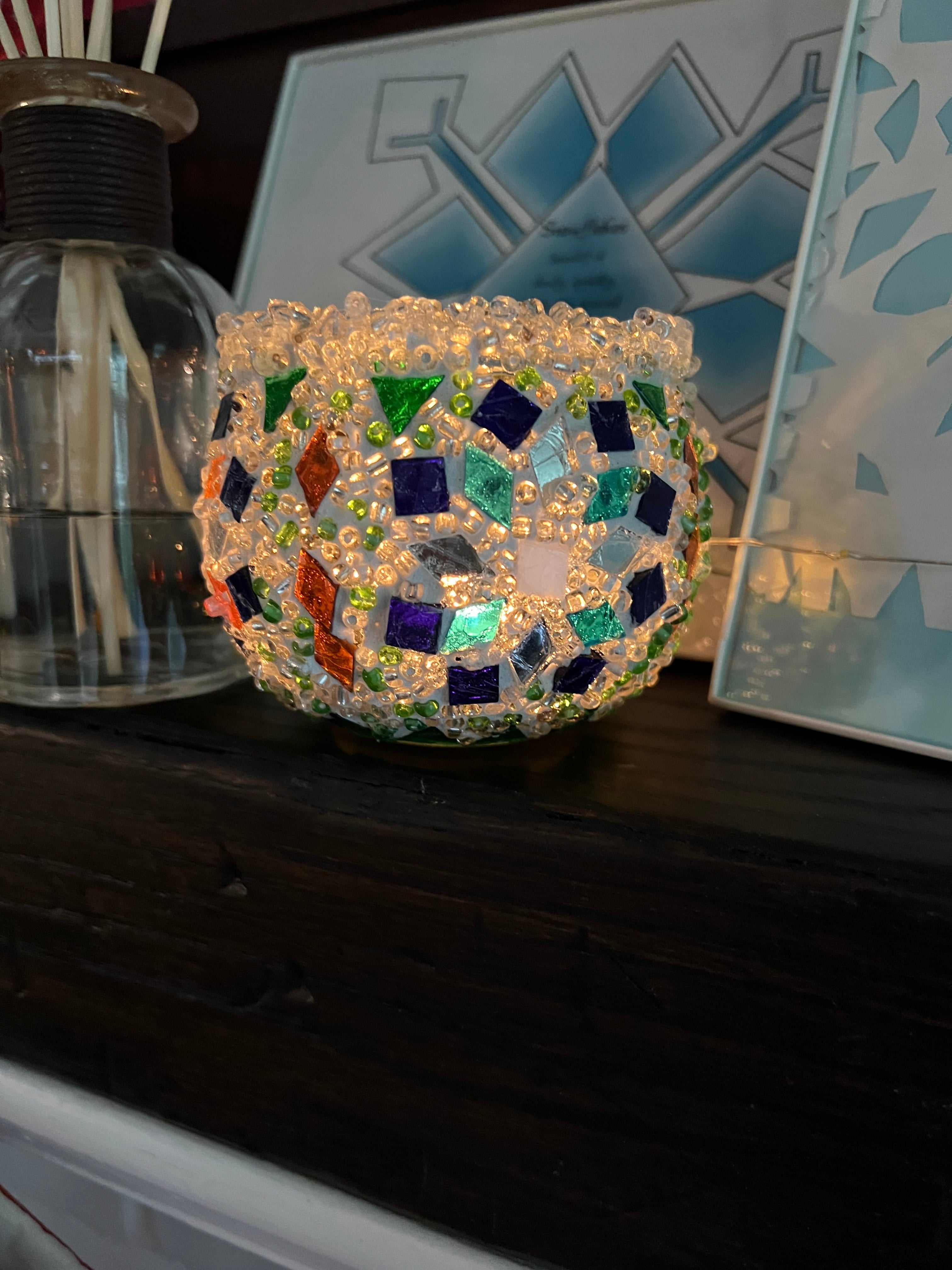 Decorative glass ball with colorful mosaic pattern on a dark surface.
