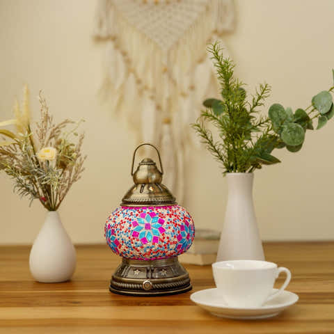 Decorative lamp with colorful mosaic design on a wooden table with vases and a cup.