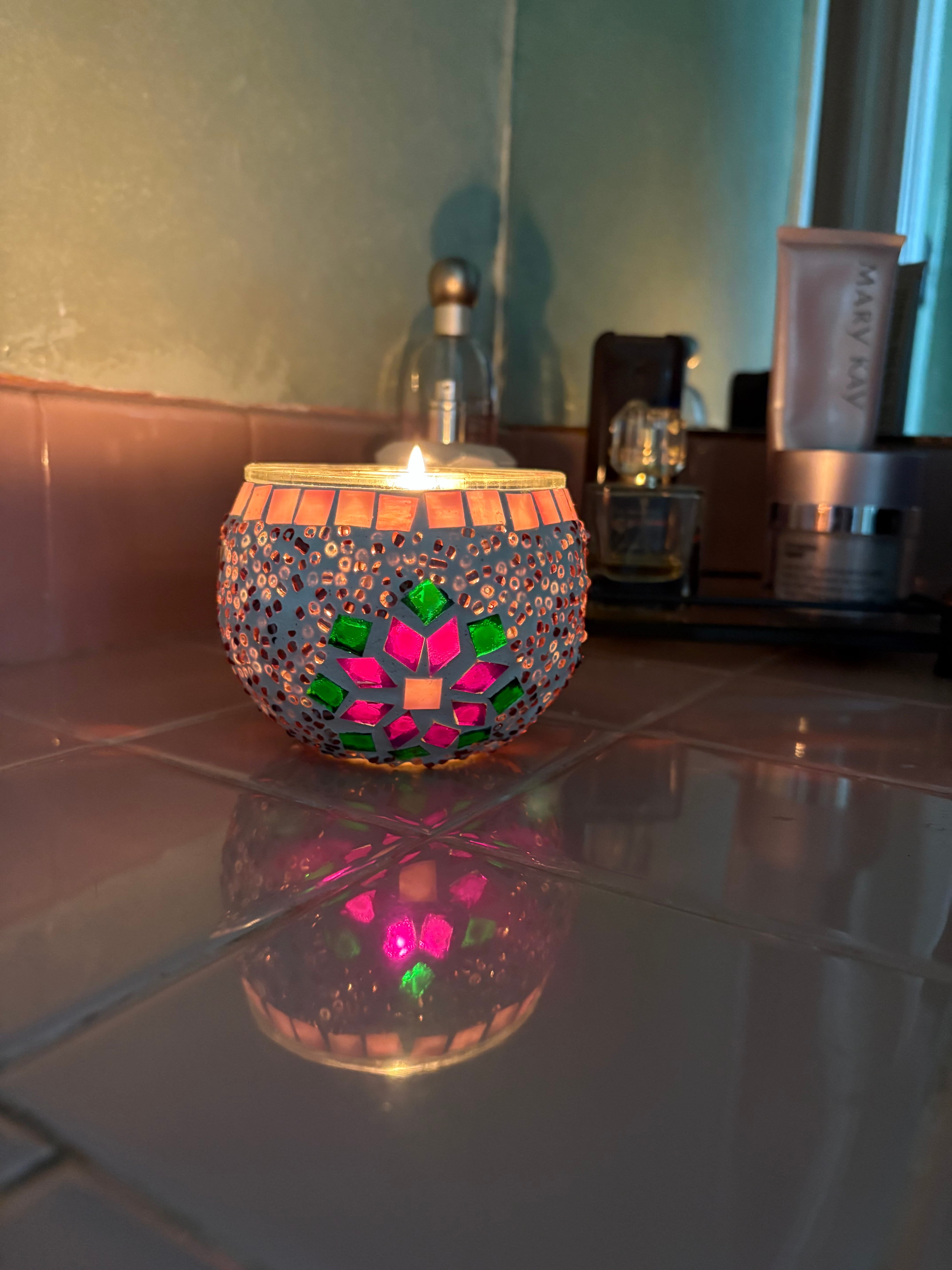 Decorative candle holder with colorful mosaic design on a reflective surface.