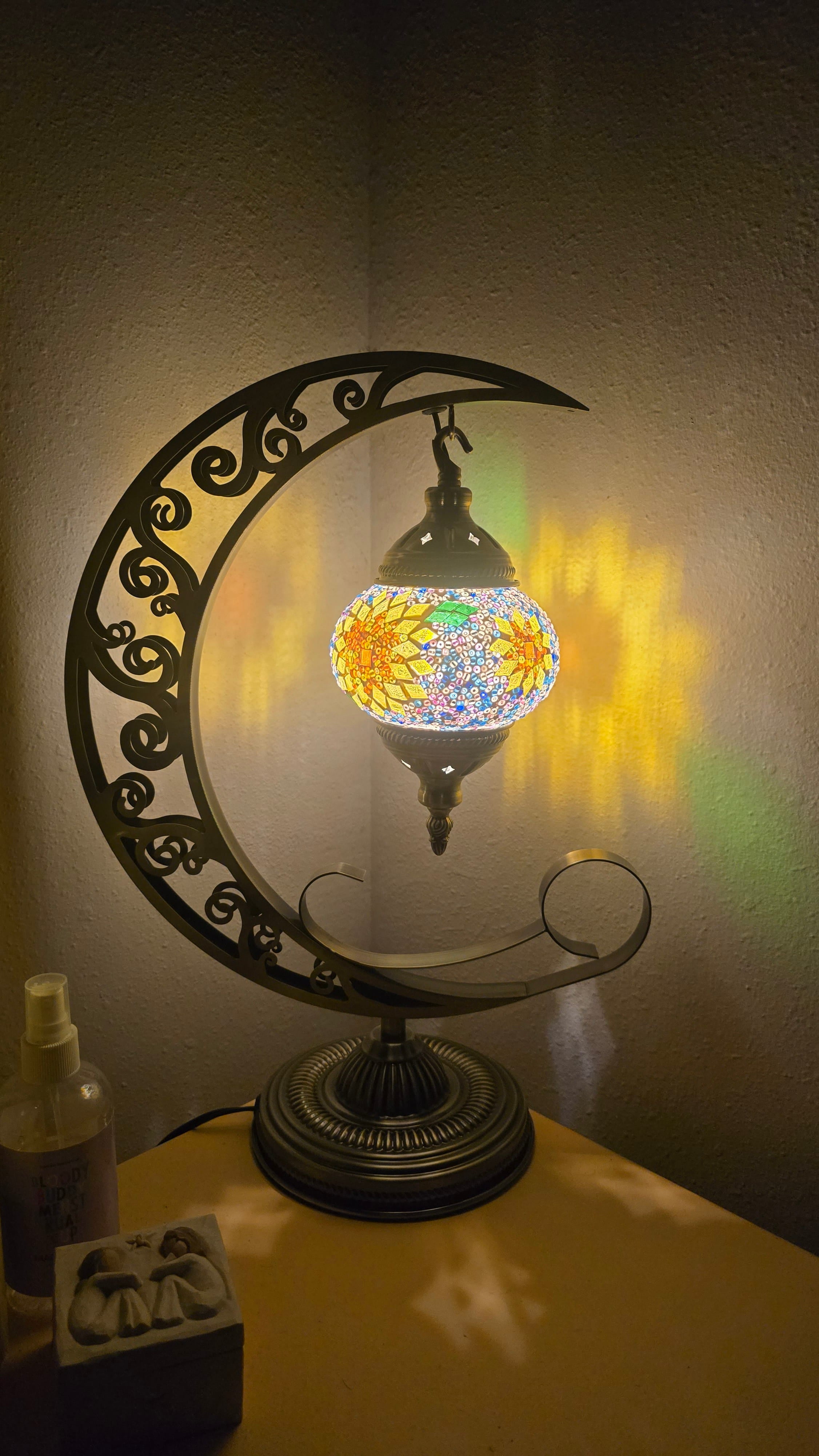 Decorative moon lamp with colorful mosaic shade on a crescent moon stand against a dark background