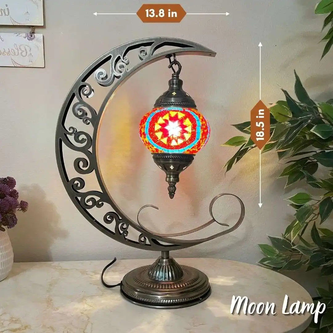 Decorative Turkish Moroccan mosaic moon lamp with colorful glass shade on a marble surface, surrounded by plants.