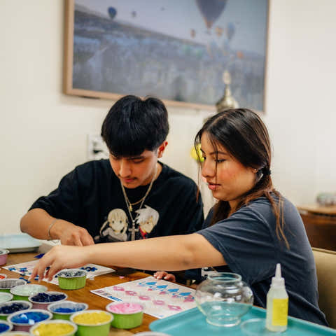 Workshop together: Two participants selecting mosaic tiles and glass pieces for their lamp project at a wooden table