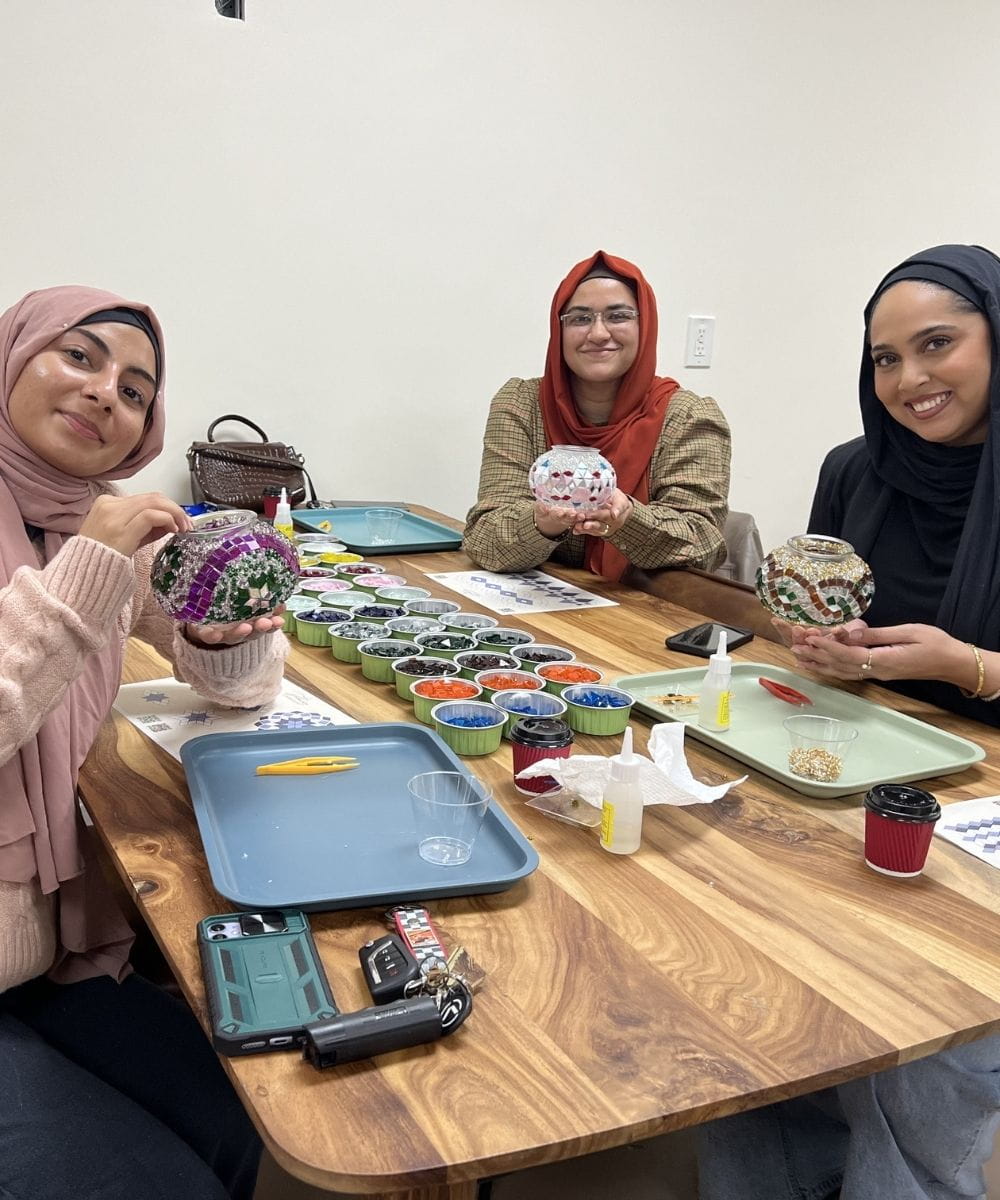 Three women sitting around a table with various items including plants and electronic devices.