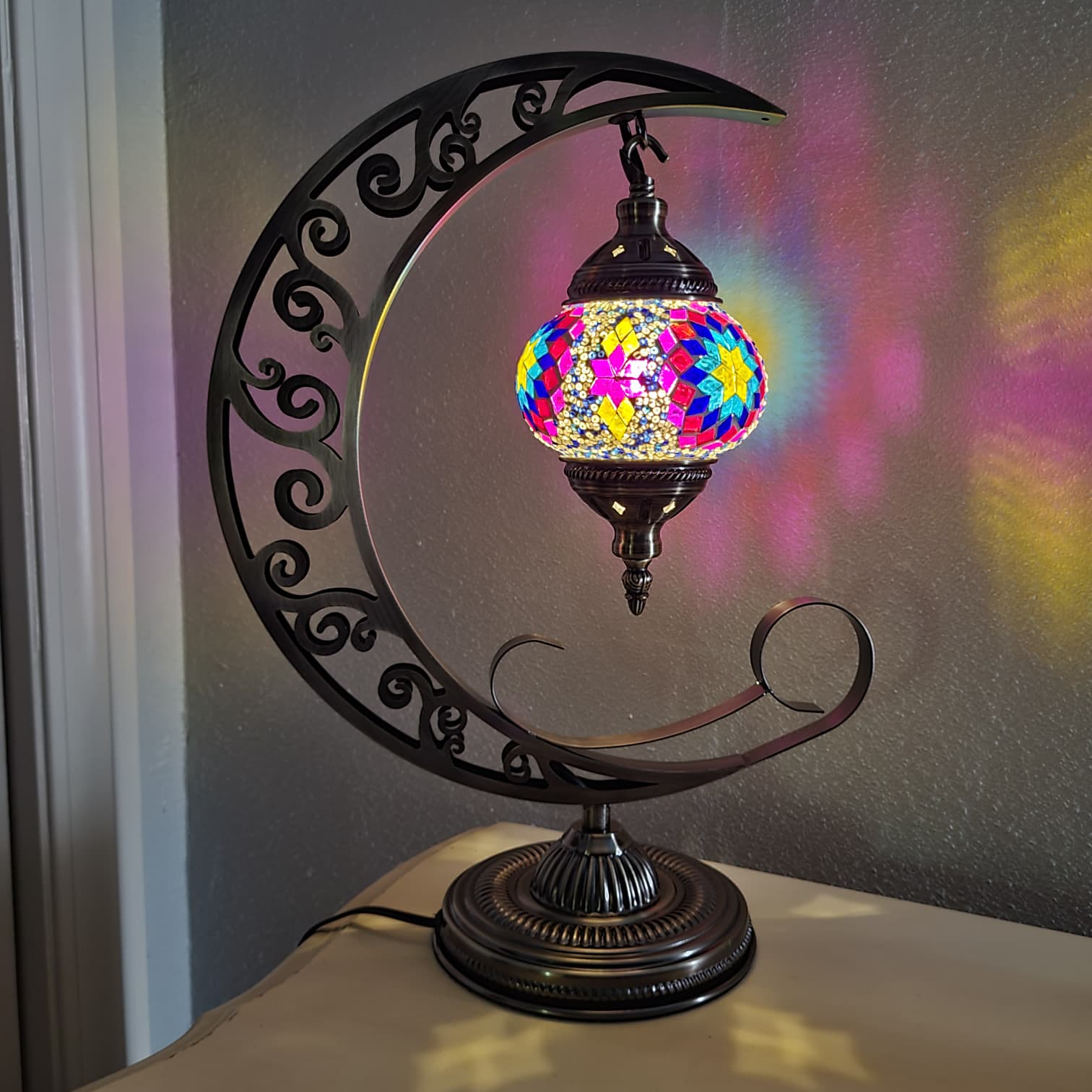 Decorative mosaic lamp with colorful glass shade on a crescent moon stand.